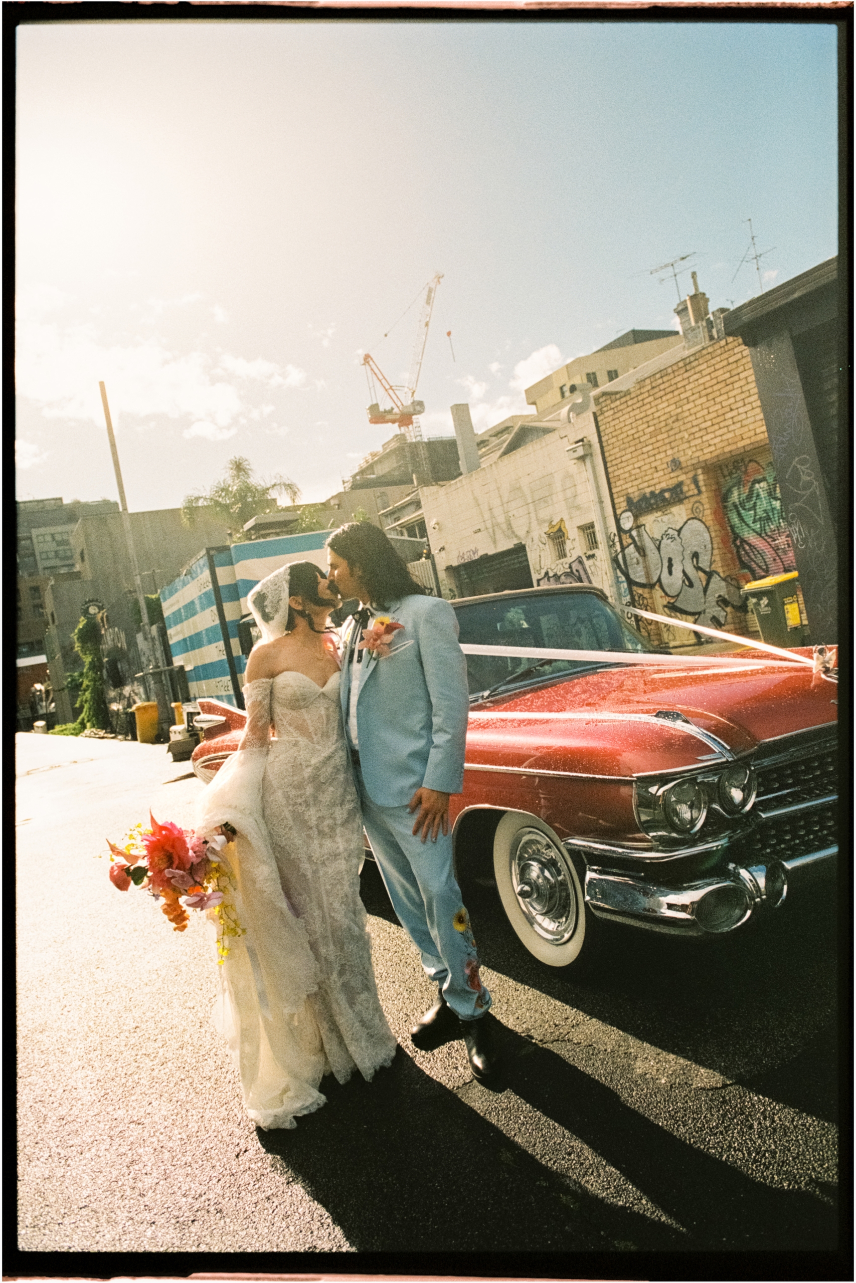 a film photo of the bride and groom kissing in fornt of their wedding car